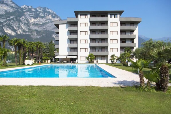 Un hôtel moderne à plusieurs étages, doté d’une piscine, entouré de palmiers et avec des montagnes en toile de fond.