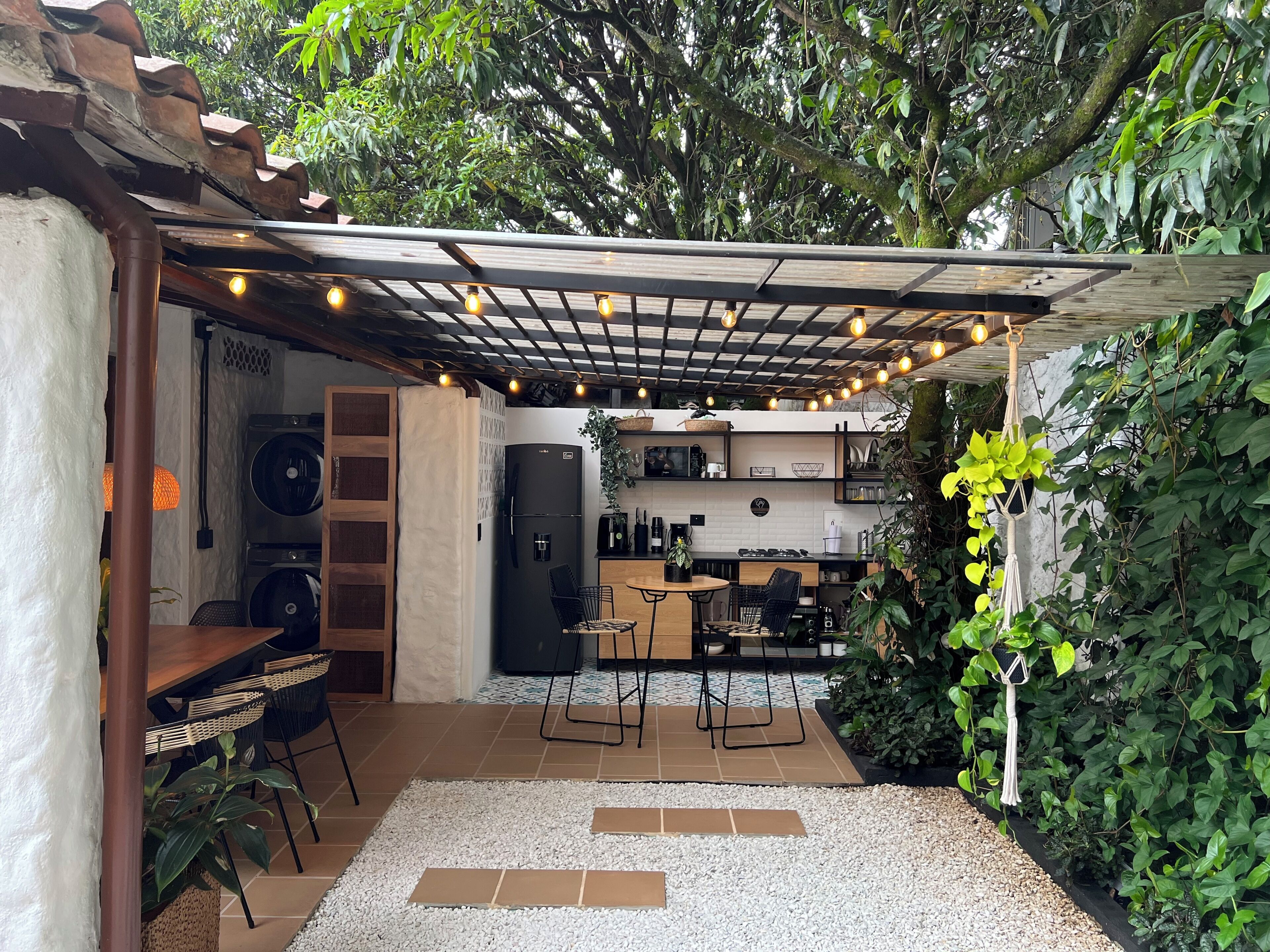 A cozy outdoor kitchen area with a pergola, string lights, and a seating arrangement.