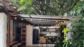 A cozy outdoor kitchen area with a pergola, seating, and a variety of plants.
