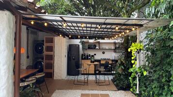 A cozy outdoor kitchen area with a pergola, string lights, and a seating arrangement.