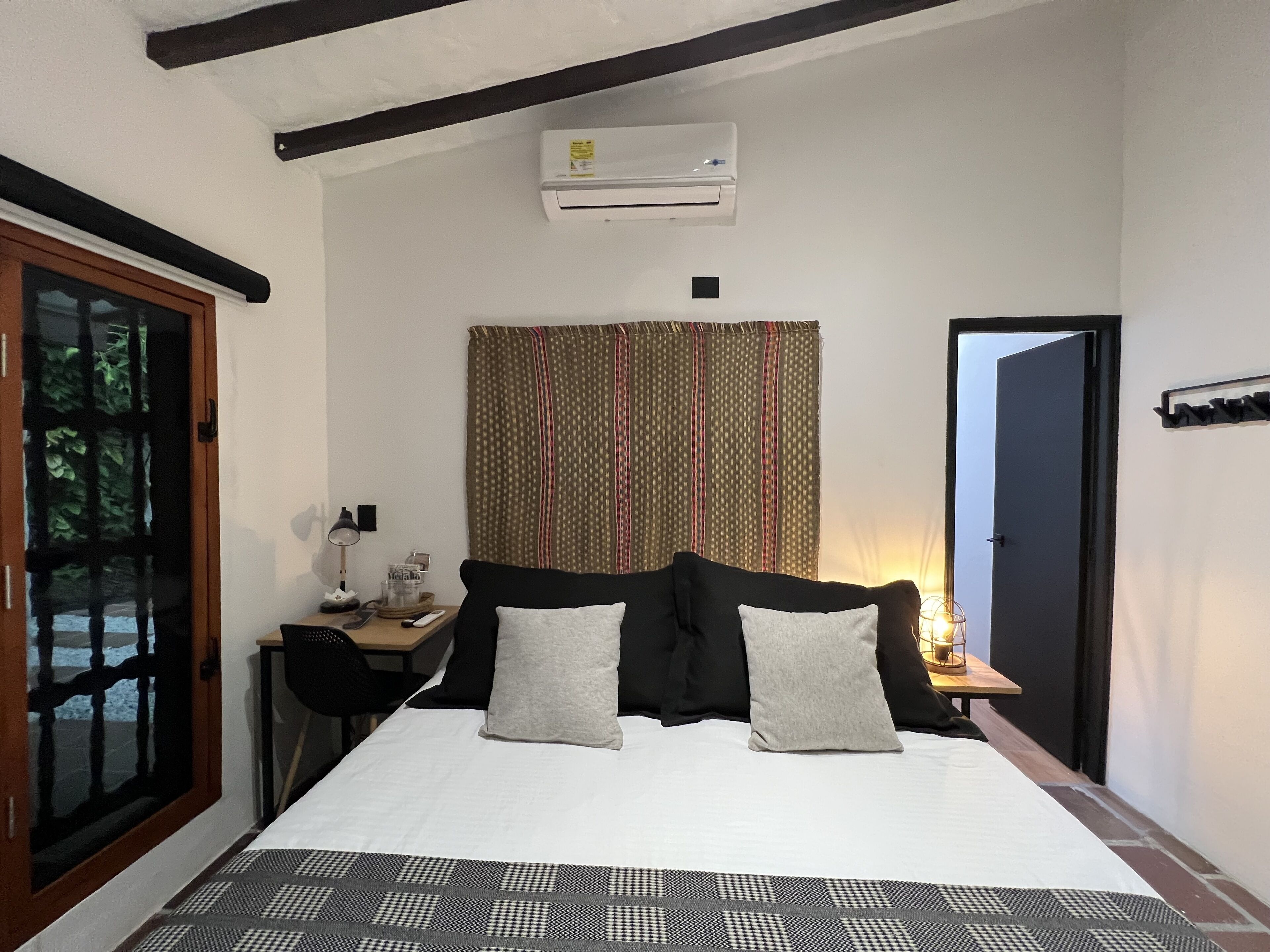 Une chambre à coucher comprenant un lit, un bureau, une chaise, une fenêtre avec des rideaux et un appareil de climatisation.