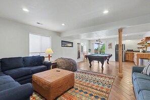 A living room with a pool table, a sofa, a coffee table, and a rug.