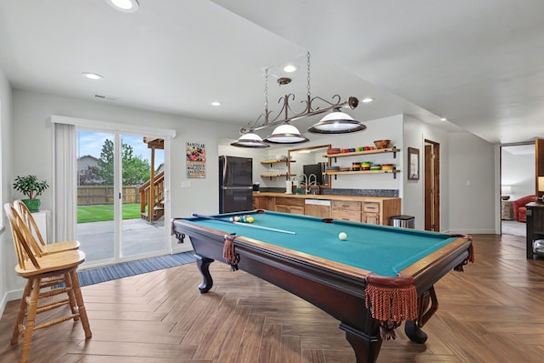 A pool table in a well-lit room with a view to the outside.