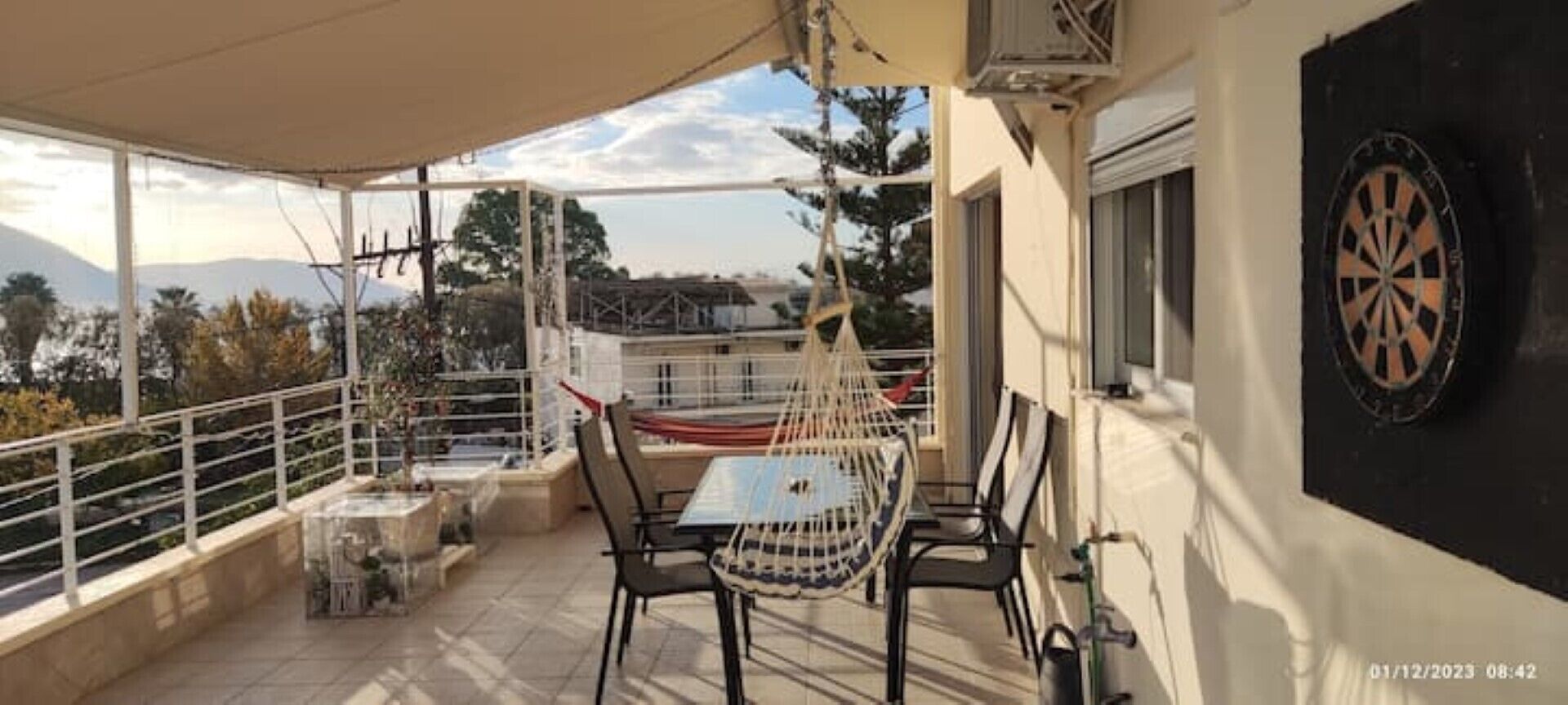 Ein Balkon mit Tisch und Stühlen, Blick auf die Berge und eine Dartscheibe an der Wand.