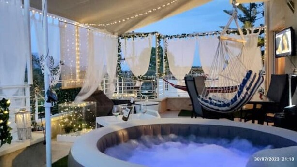 A hot tub in a tented area with string lights, a hammock, and a view of a cityscape. - Άνετο παραθαλ άσσιο διαμέρισμα με υδρομασάζ , δέκα λεπτά  από τους Δελφούς ! (Itea)