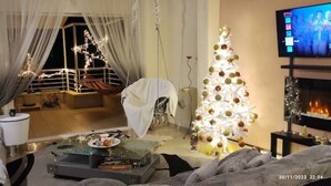 A cozy living room with a Christmas tree, a fireplace, and a television. - Άνετο παραθαλάσσιο διαμέρισμα με υδρομασάζ , δέκα λεπτά  από τους Δελφούς ! (Itea)