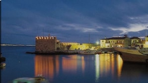 A coastal town with a historic stone tower, waterfront buildings, and boats docked at the harbor. - Άνετο παραθαλάσσιο διαμέρισμα με υδρομασάζ , δέκα λεπτά  από τους Δελφούς ! (Itea)