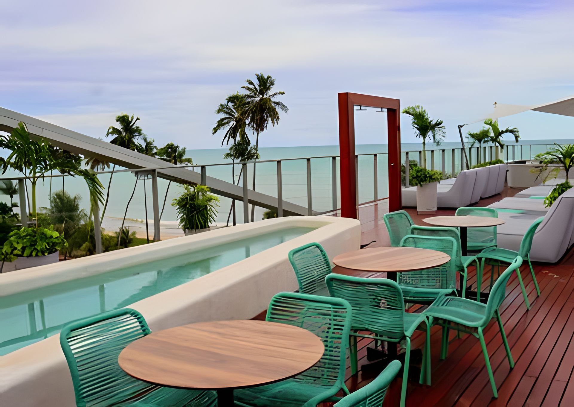 A rooftop terrace with a pool, green chairs, and a view of the ocean.