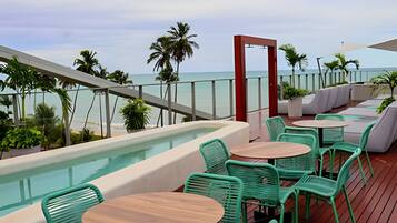 A rooftop terrace with a pool, green chairs, and a view of the ocean.