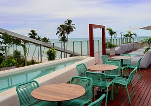 Terraço no telhado com piscina, cadeiras verdes e vista para o oceano.