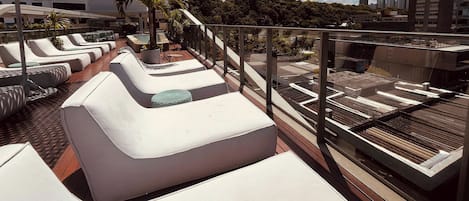 A rooftop lounge area with sun loungers and a pool.