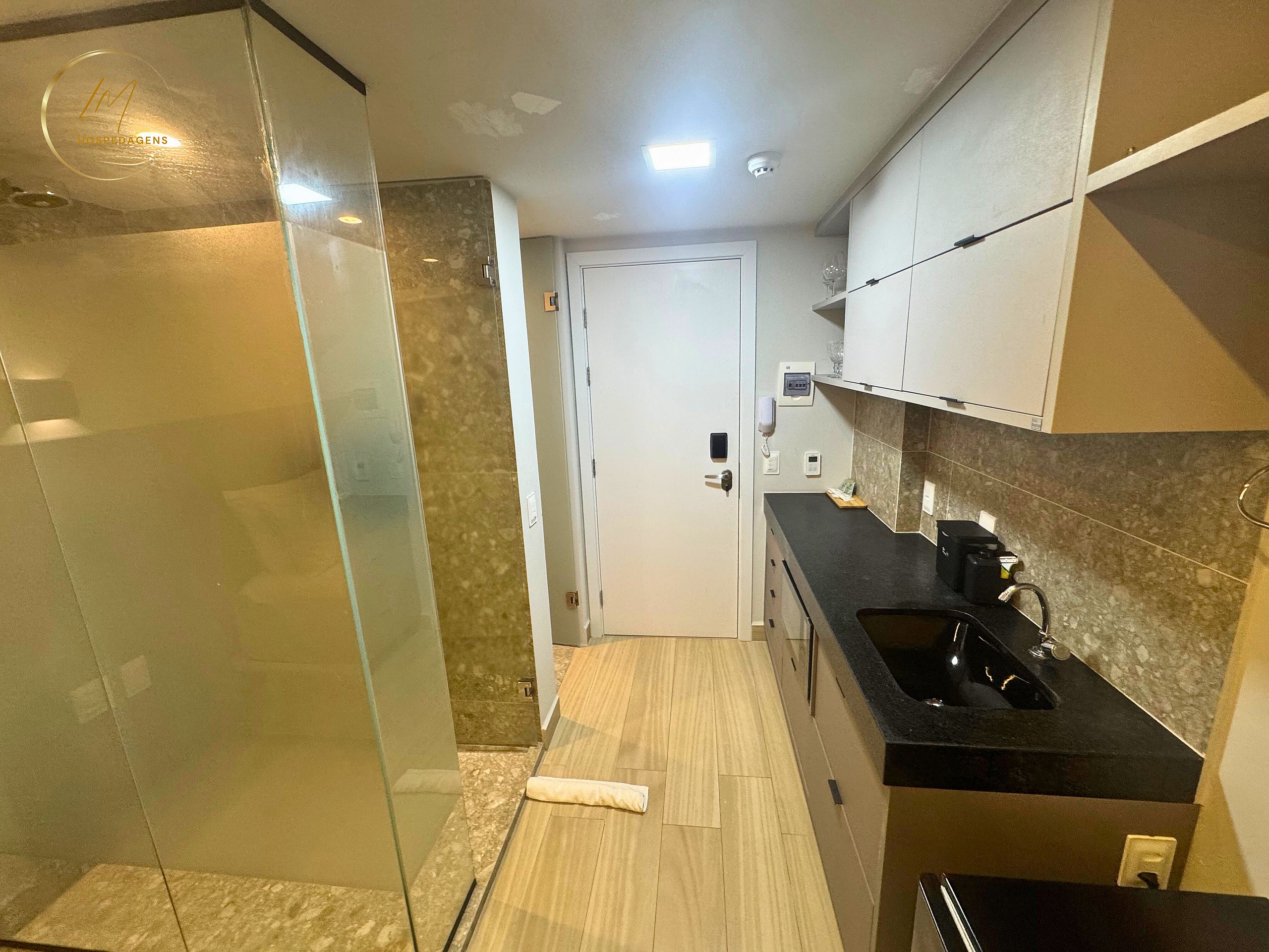 Un couloir étroit comprenant une douche, une porte, un coin cuisine avec un évier et un plan de travail.