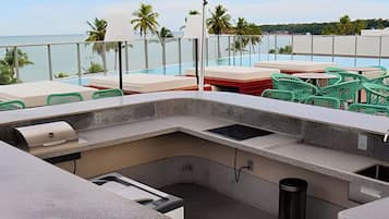 A poolside area with a concrete bar, a trash bin, and green plastic chairs.