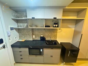 Una cocina compacta con microondas, un lavamanos y un refrigerador negro. Hay armarios sobre la encimera y un teléfono en la pared.