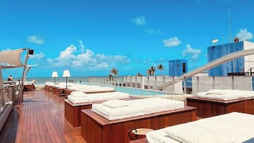 Una terraza soleada con piso de madera, asientos blancos acolchados y una vista despejada del océano.