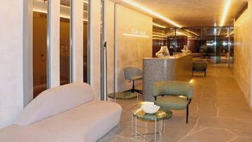 Un moderno vestíbulo de hotel con mostrador de recepción, zona de estar y puertas de vidrio que dan a las habitaciones.