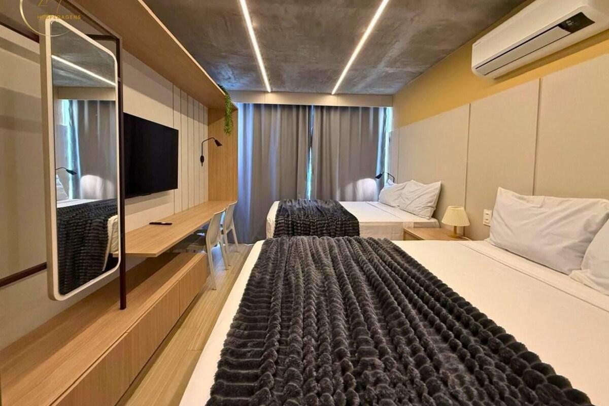 Quarto de hotel moderno com uma cama grande, televisão, espelho e ar condicionado.