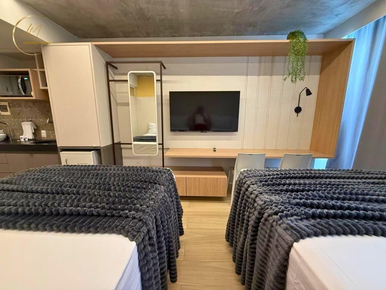 Una habitación de hotel moderna con dos camas, televisión, un escritorio pequeño y una kitchenette.