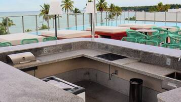 A rooftop bar with a view of the ocean, outdoor seating, and a grill.