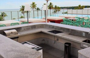 A rooftop bar with a view of the ocean, outdoor seating, and a grill. - LM Setai Yacth (João Pessoa)