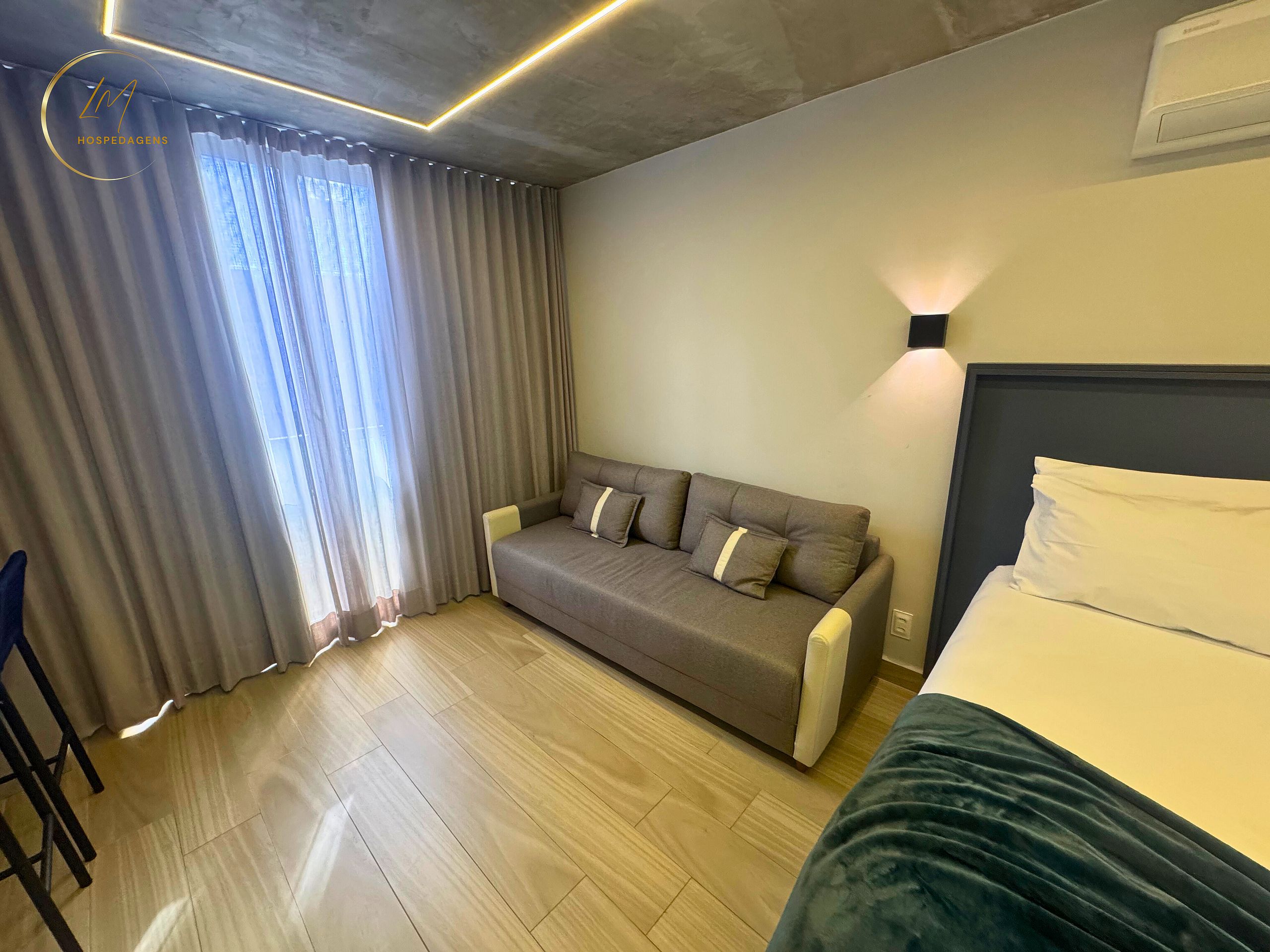A hotel room with a sofa, a bed, a chair, and a window with curtains.