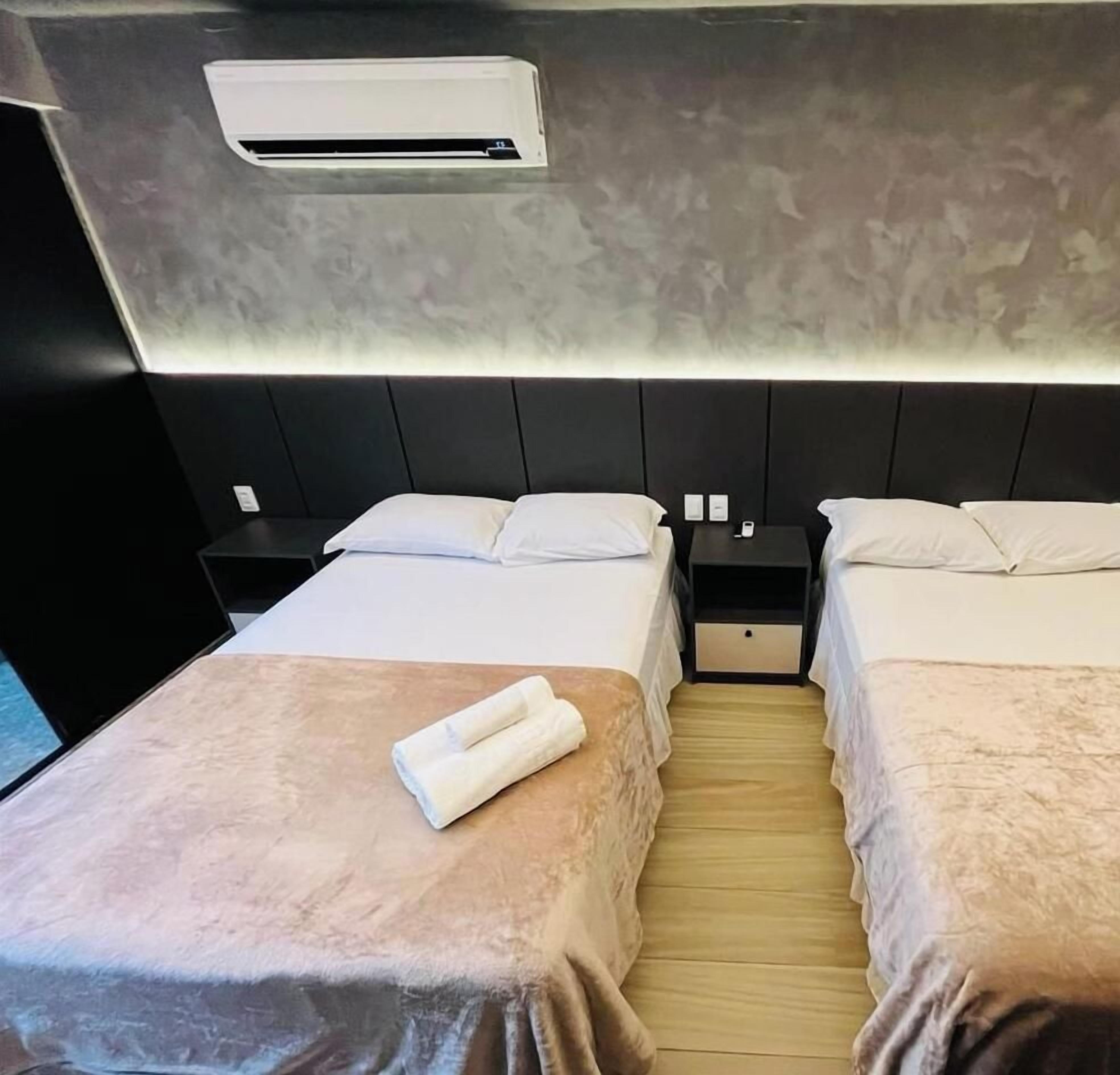 Una camera d'albergo con due letti, un comodino, un condizionatore d'aria e un pavimento in legno.