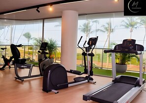 Un gimnasio con máquinas de cardio, una cinta de correr y amplias ventanas con vista a palmeras.
