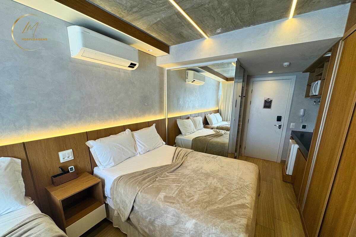 Una habitación de hotel moderna con una cama grande, mesitas de noche, un espejo y un equipo de aire acondicionado.