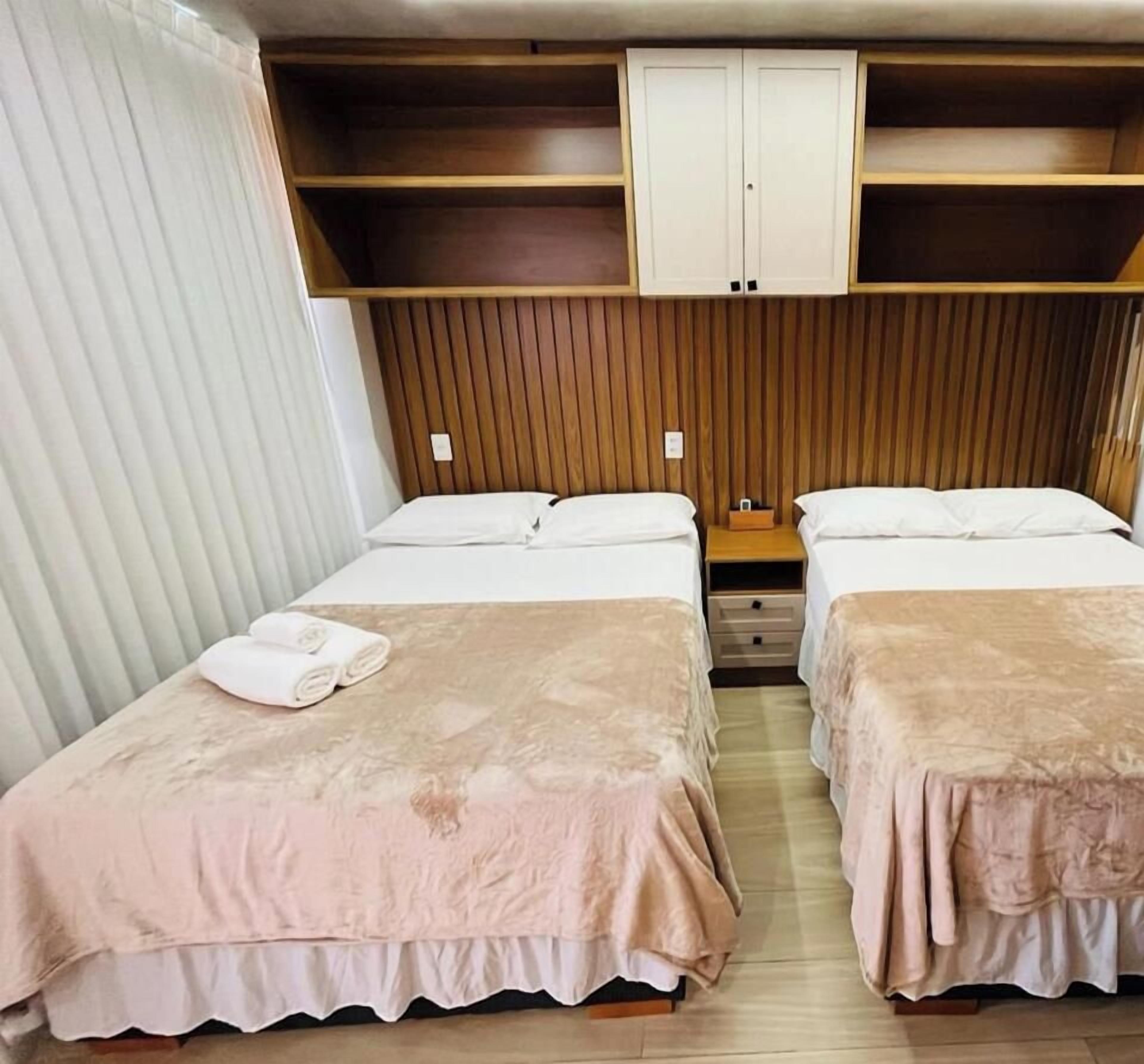 A room with two beds, a wooden wardrobe, and a small table with a lamp.