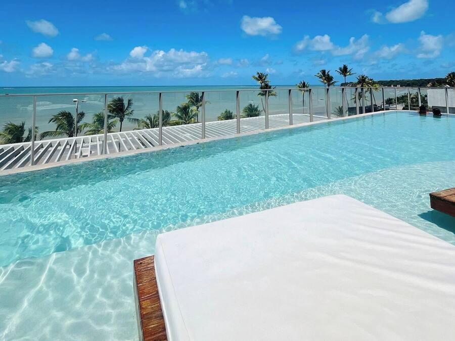 A clear blue swimming pool with a white lounge area and a view of the ocean.