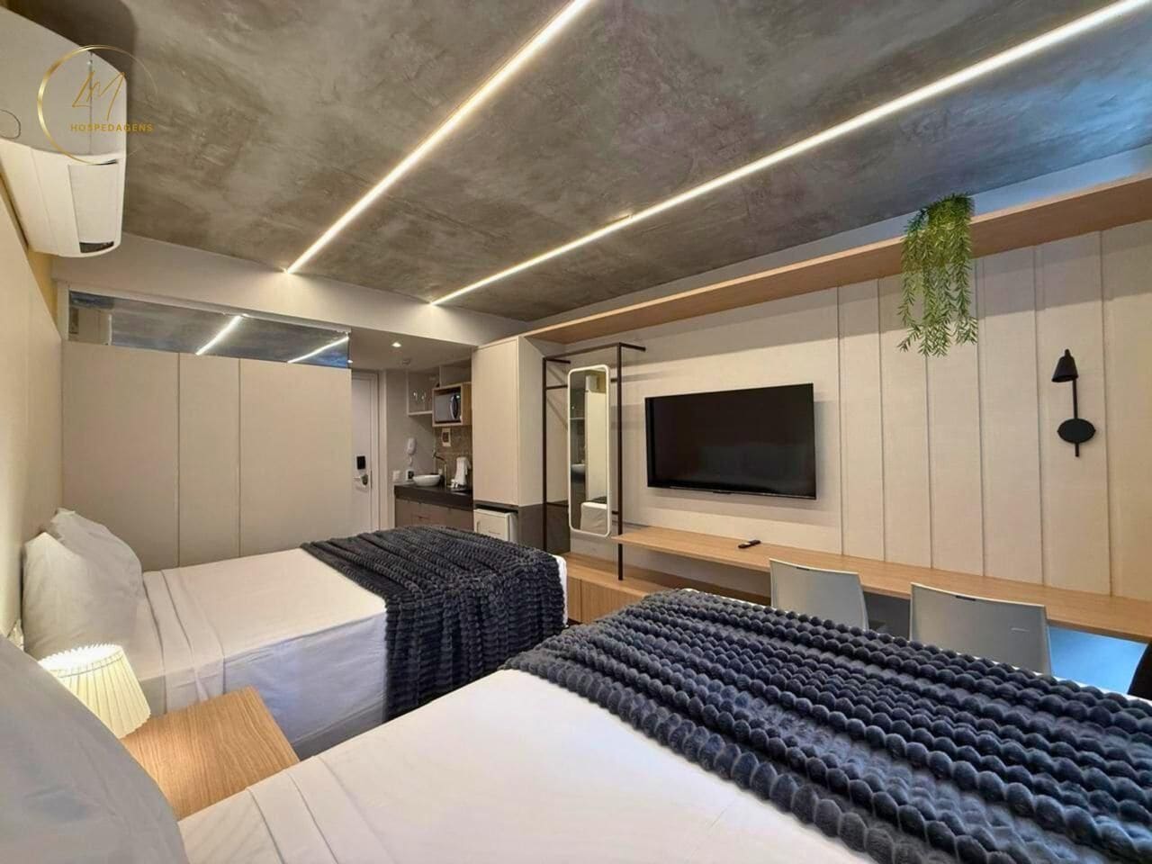 Quarto de hotel moderno com duas camas, uma televisão, uma escrivaninha e um banheiro.