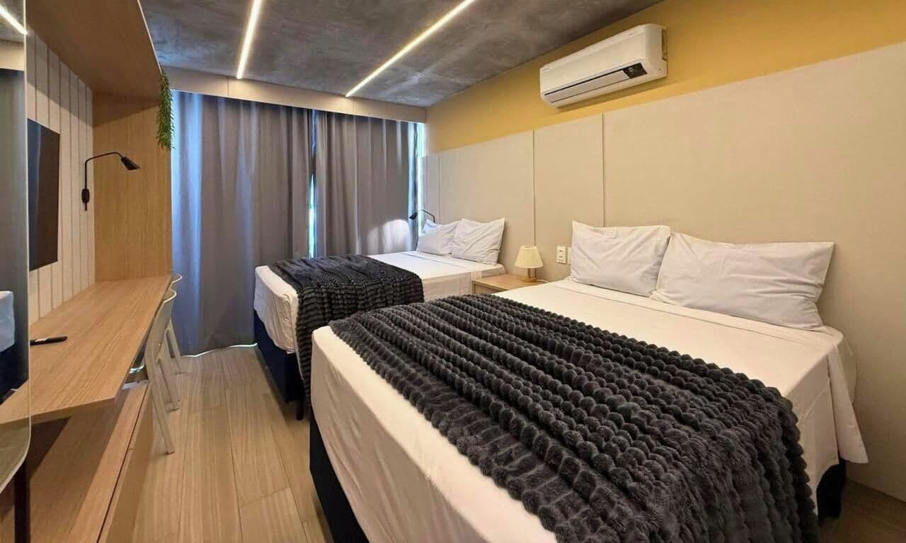 A hotel room with two beds, a desk, and an air conditioning unit.