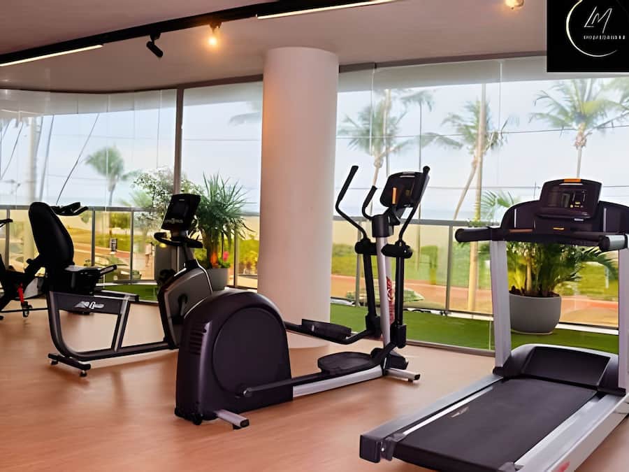 A gym with cardio machines, a treadmill, and large windows with a view of palm trees.