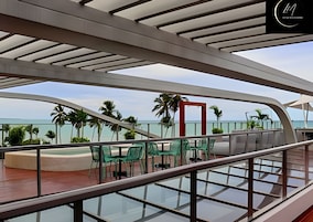 Um deck moderno com guarda-corpos de vidro, cadeiras verdes e vista para o oceano.