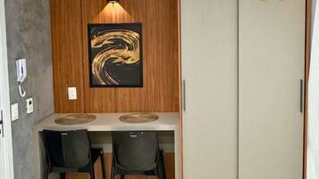A room with a wooden wall panel, a framed artwork, a desk with two chairs, and a wardrobe with a circular logo.