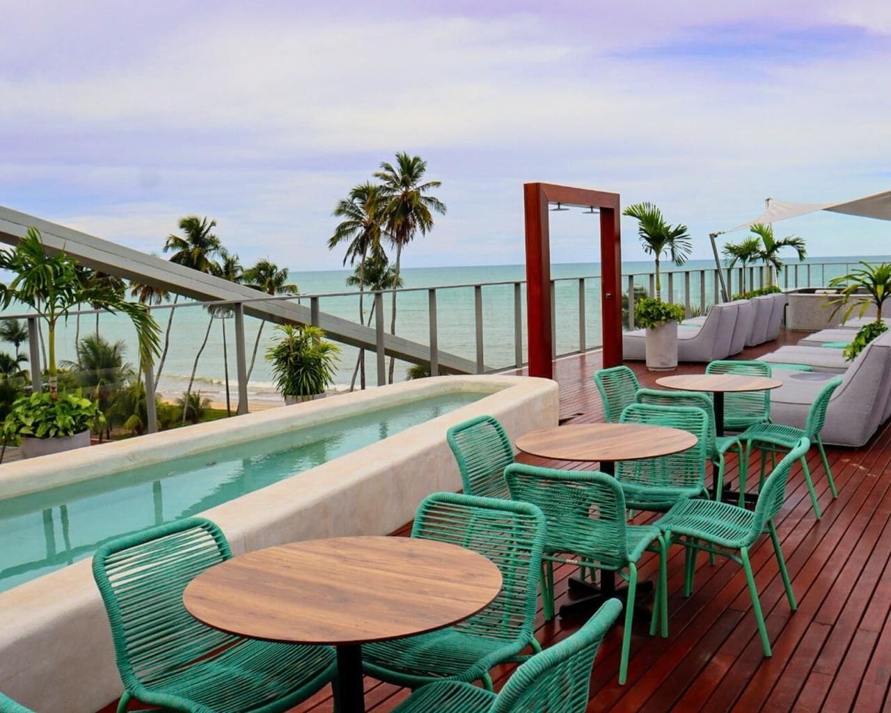 Um bar no terraço com piscina, cadeiras verdes e vista para o oceano.