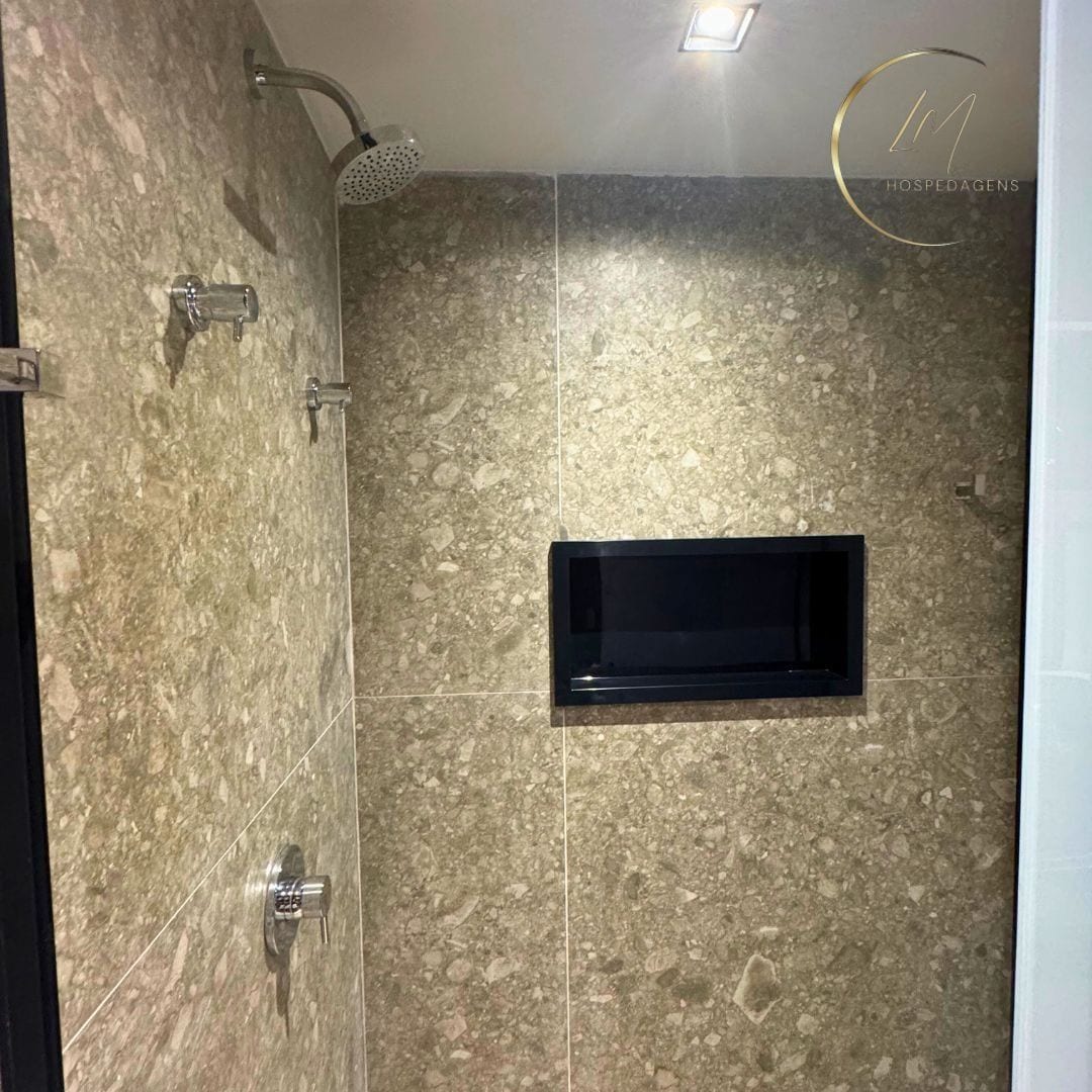 Un baño con ducha, un espejo pequeño con marco negro y pared de mármol.