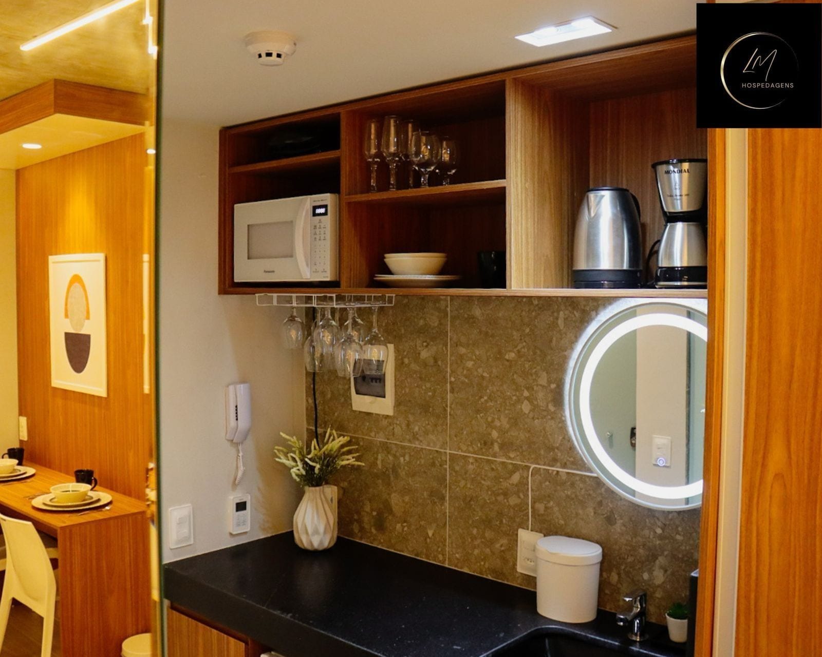 A compact kitchen with a microwave, coffee maker, and wine glasses on shelves.