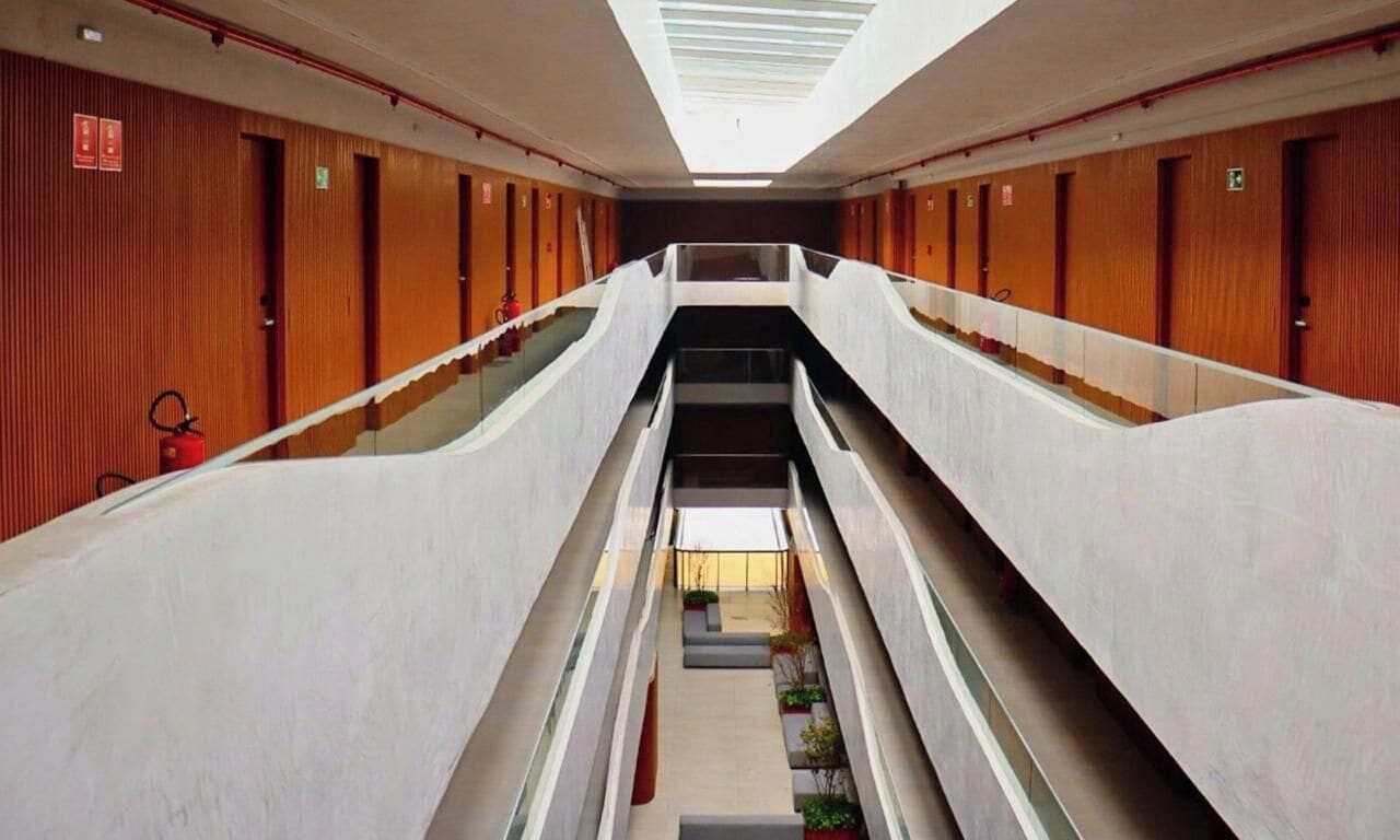 Interior de hotel con varios niveles, una escalera central, paneles de madera en las paredes y un tragaluz.
