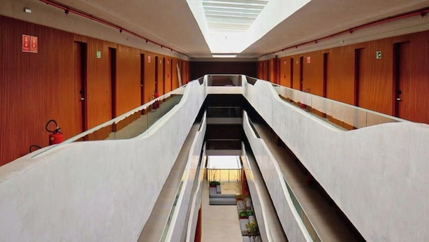 Un intérieur d’hôtel à plusieurs niveaux, avec un escalier central, des lambris en bois sur les murs et une verrière au plafond.
