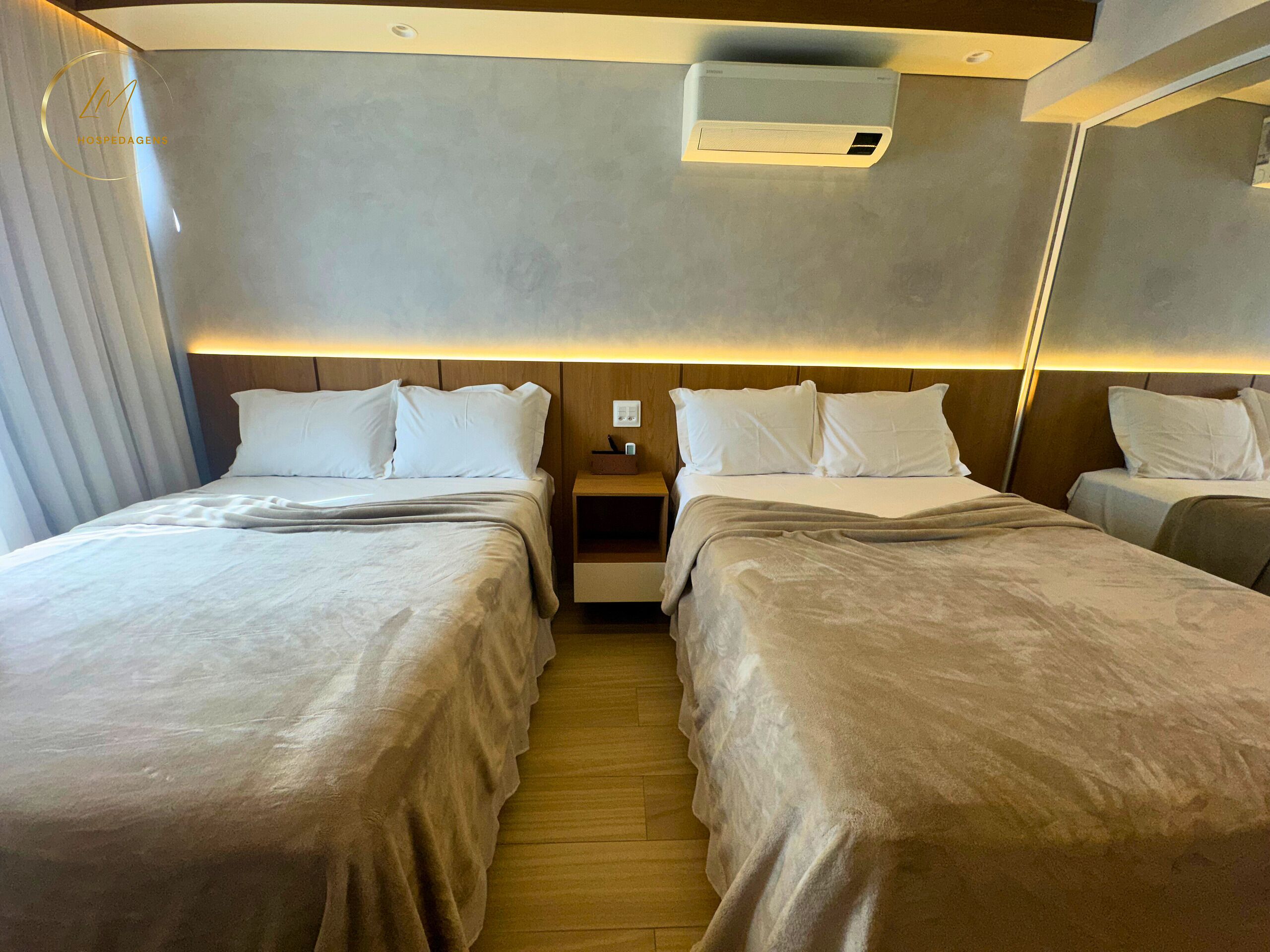 Habitación de hotel con dos camas, una mesita de noche, un equipo de aire acondicionado y un espejo en la pared.