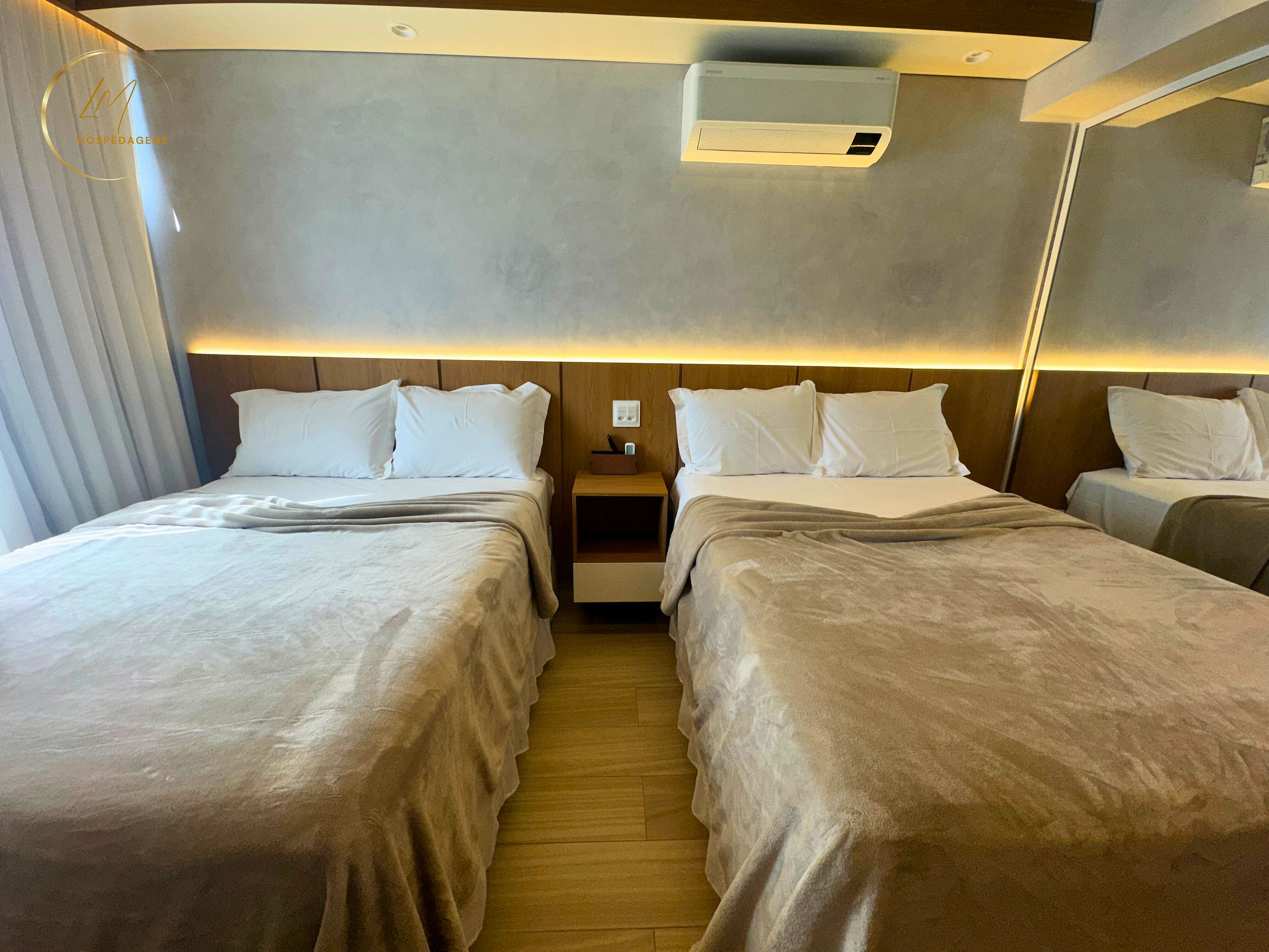 Ein Hotelzimmer mit zwei Betten, einem Nachttisch, einer Klimaanlage und einem Spiegel an der Wand.