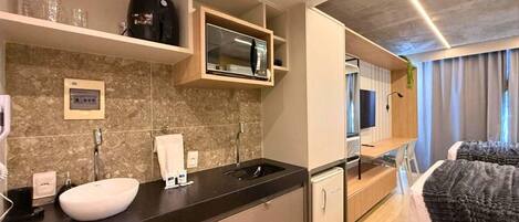 A modern hotel room with a kitchen area, a bed, and a TV.