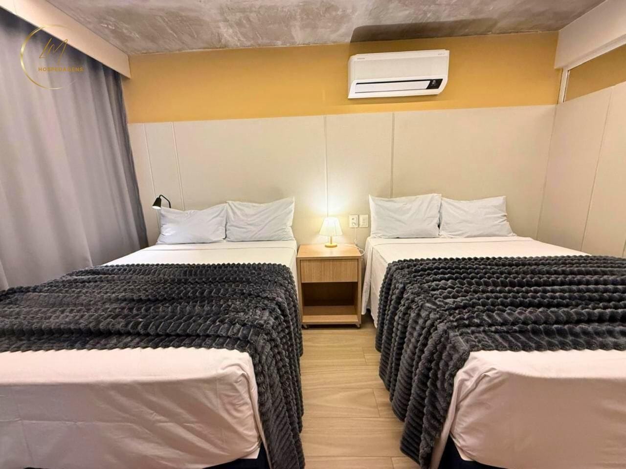 A hotel room with two beds, a nightstand with a lamp, and an air conditioning unit on the wall.