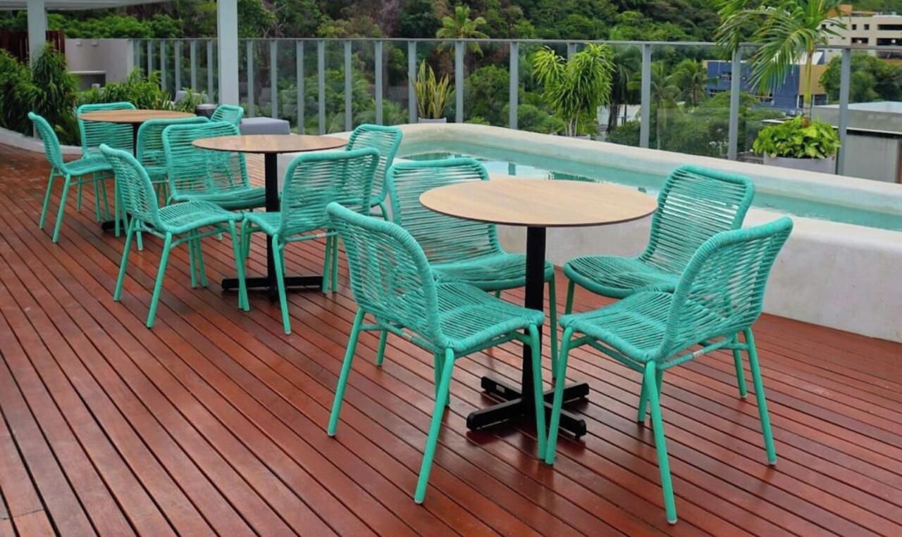 Une terrasse sur le toit, dotée d'un plancher en bois, de meubles en osier vert et offrant une vue sur la verdure et les bâtiments.