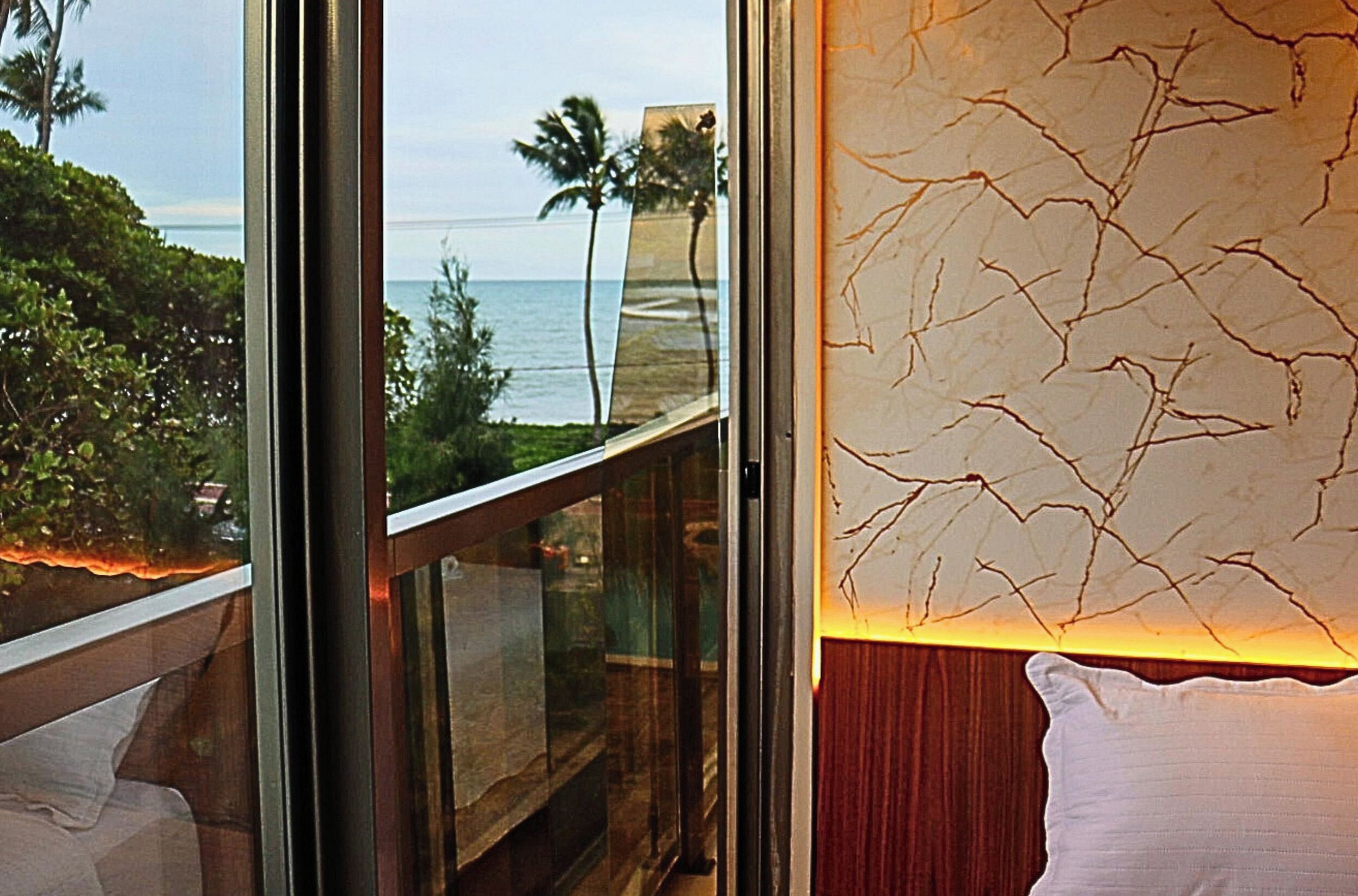 A room with a large window overlooking a beach, a wooden balcony, and a textured wall.