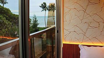 A room with a large window overlooking a beach, a wooden balcony, and a textured wall.