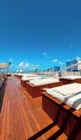Um deck ensolarado com piso de madeira, cadeiras de estar e área de piscina.