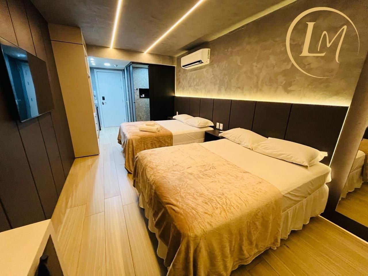 Habitación de hotel con dos camas, piso de madera, aire acondicionado de pared y un logotipo en la pared.