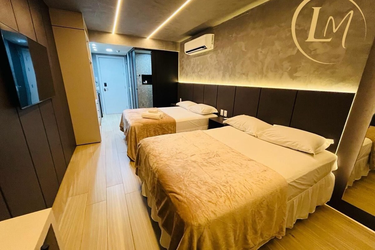 Quarto de hotel com duas camas, piso de madeira, ar condicionado fixado na parede e um logotipo na parede.
